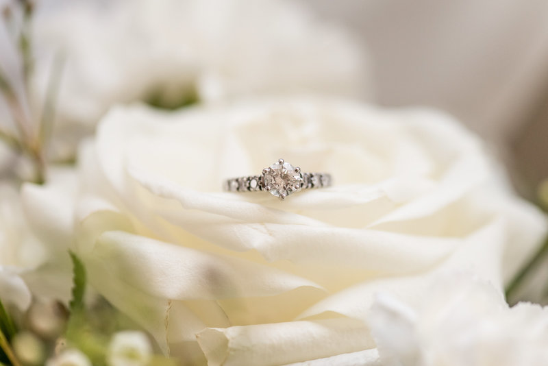 A simple diamond ring sits on a white rose
