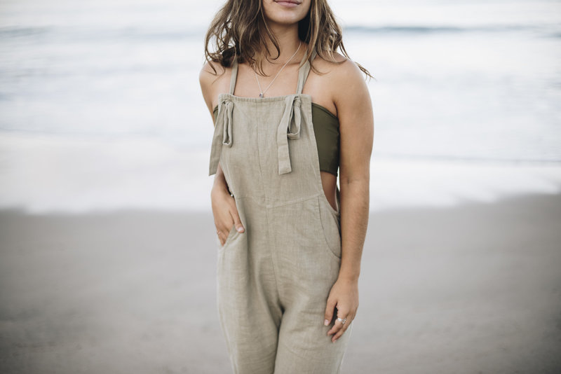 Close up of woman's torso wearing canvas overalls on beach during brand photo shoot
