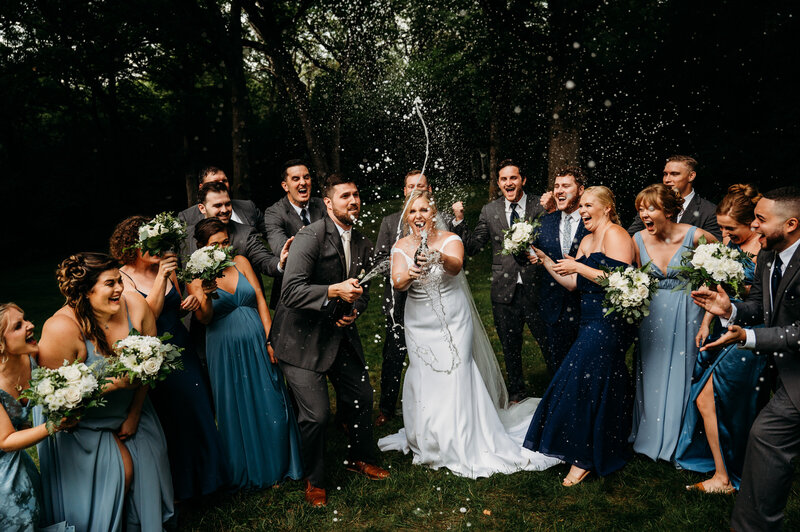 Bride and groom spraying champagne while bridal party cheers