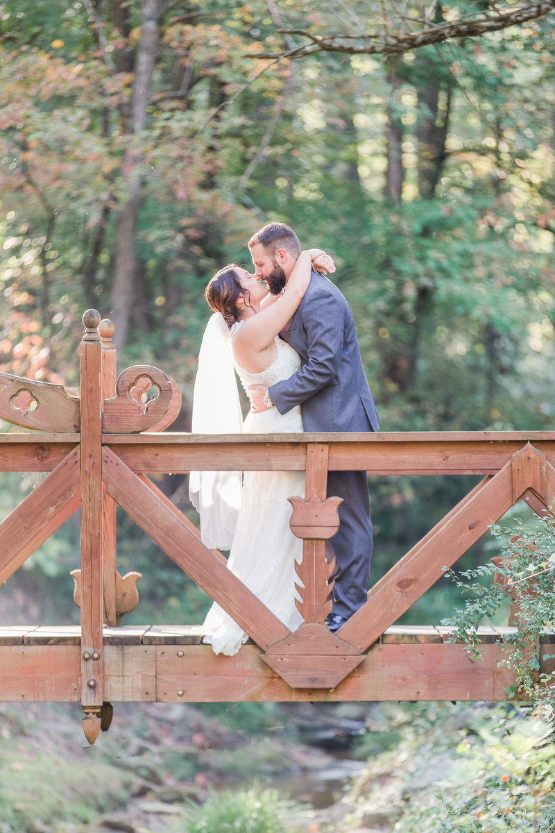 Bride and groom embrace on a bridge while kissing on their wedding day