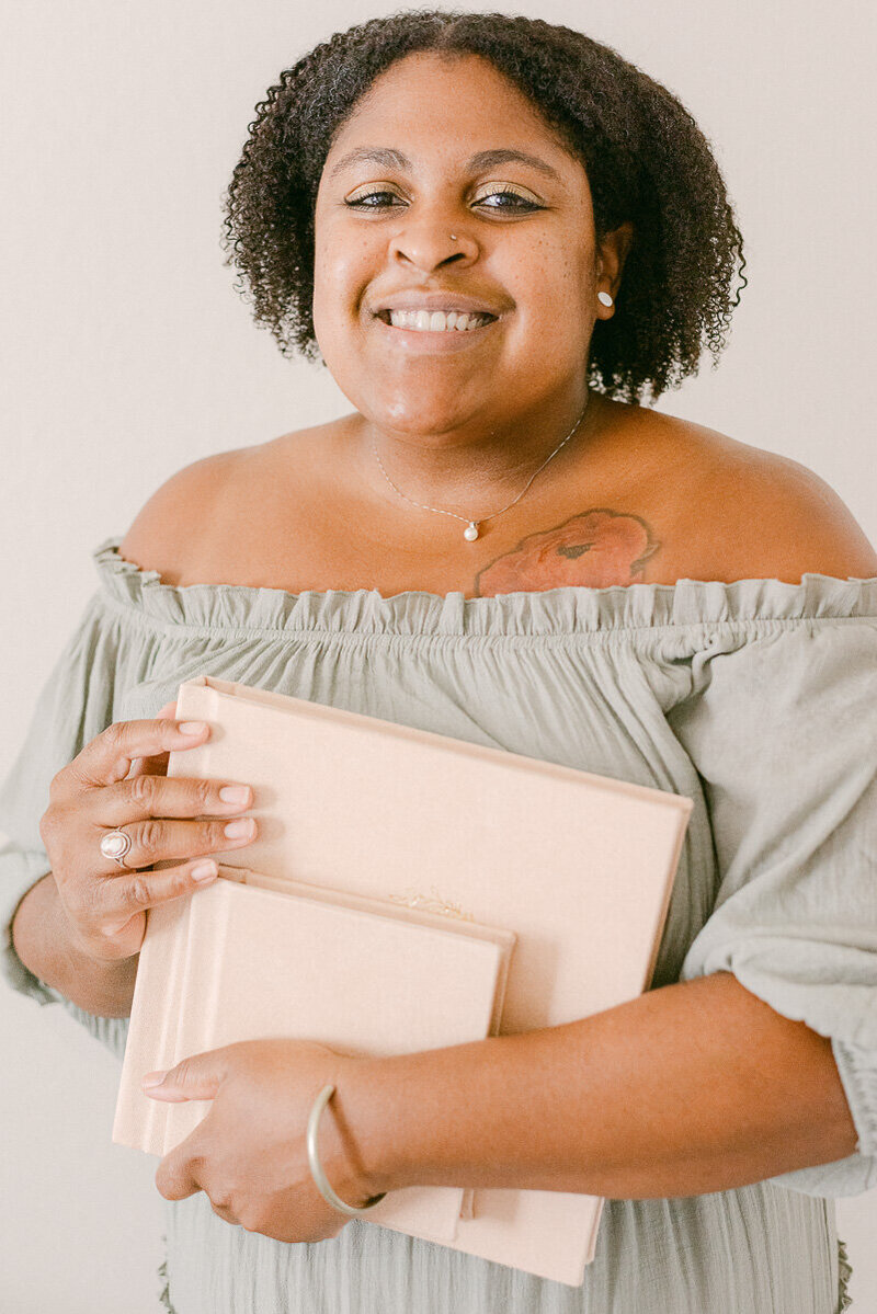 Jasmyn Coleman  phoenix photographer holding heirloom albums and smiling at camera.