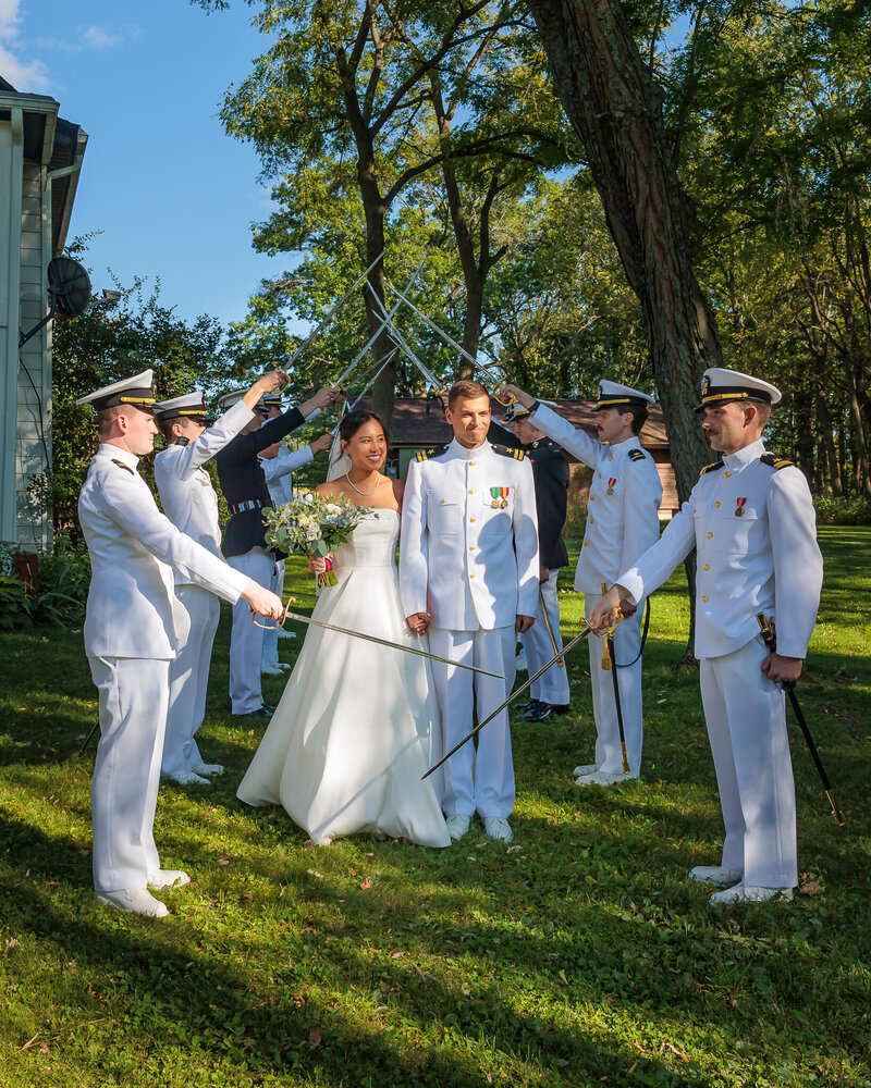 Bride and groom walk under a ceremonial arch of swords held by uniformed officers during an outdoor wedding at Barnwood Events in Madison, Wisconsin.