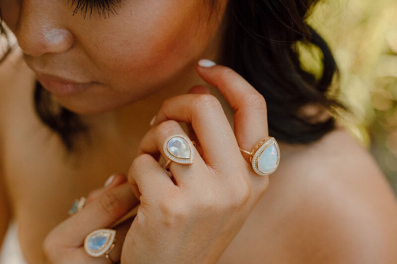 Model wearing moonstone and opal rings with full natural diamond halos
