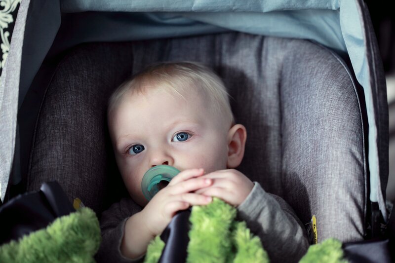 Baby in travel seat with green pacifier