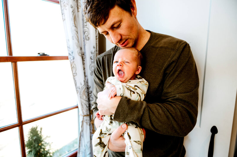 newborn baby yawning as dad hold him in the nursery