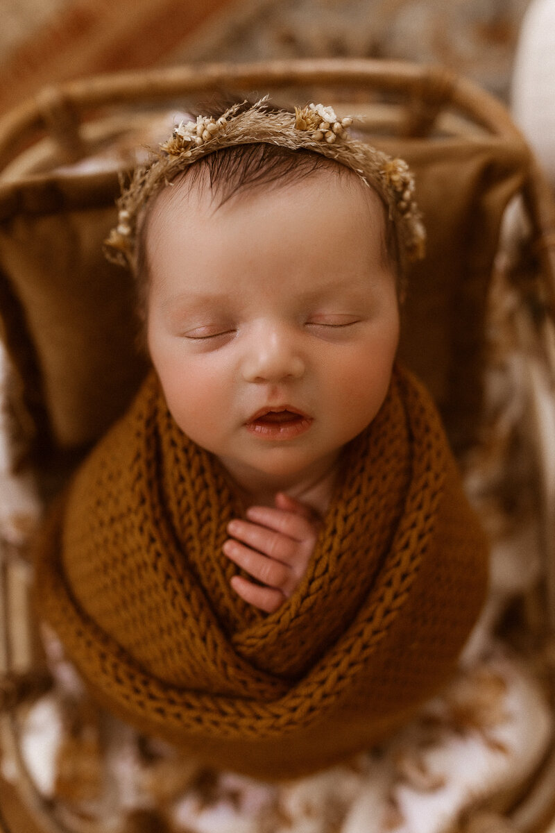 Newborn baby girl wrapped up in a crochet blanket with a flower crown