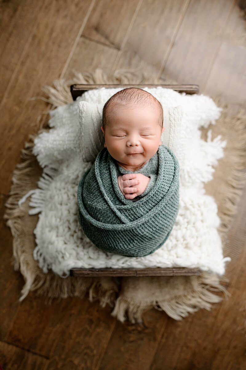 newborn  wrapped in cream laying on a bed 