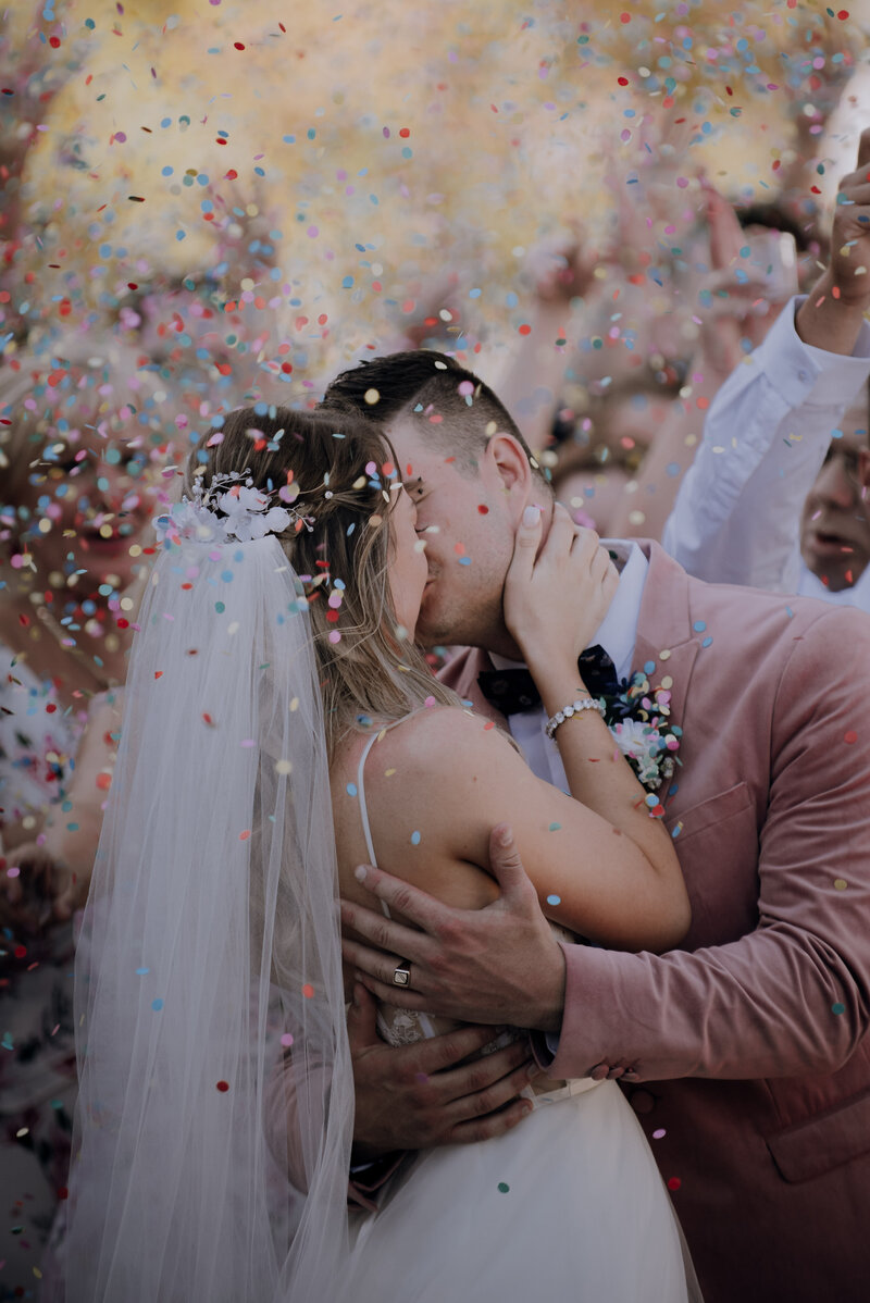 Just married couple kissing in a cloud of falling confetti