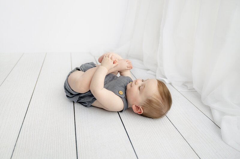 little 7 month old boy lays on his back playing with his feet