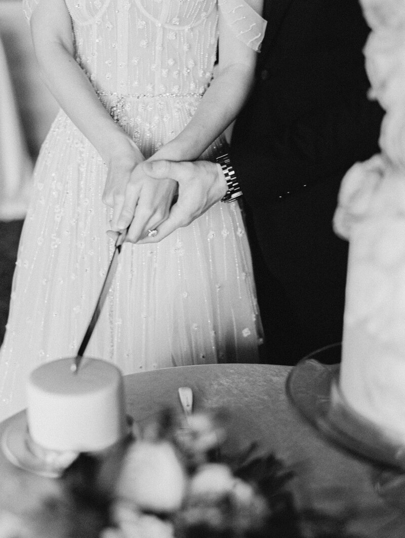 Bride and groom hold knife to cut reception cake together