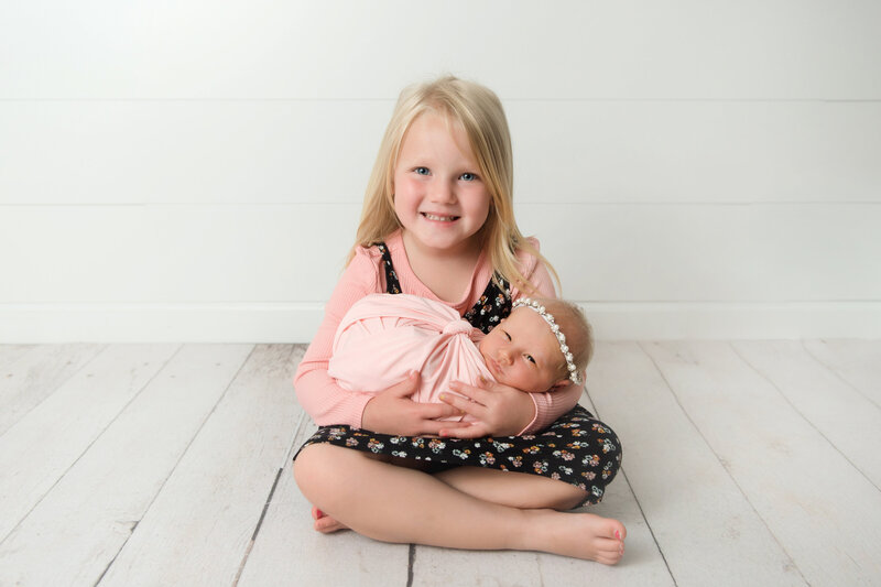 Toddler girl holding newborn baby sister during newborn portrait session.