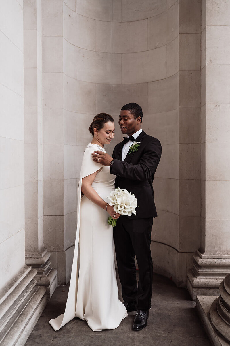 groom fondly touches bride’s shoulder as they face each other and pose in an alcove of the marylebone town hall where they had their wedding ceremony