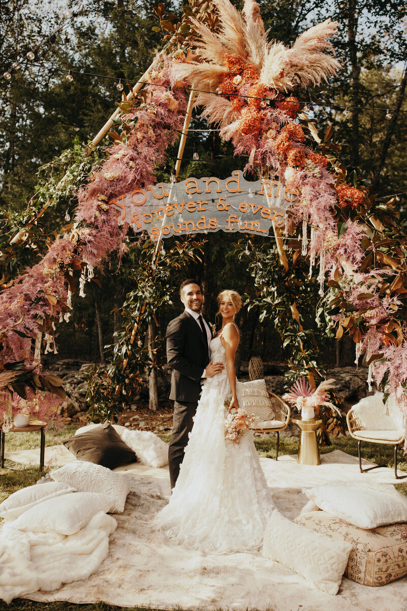 bride and groom under pink pampas floral tee pee with neon sign