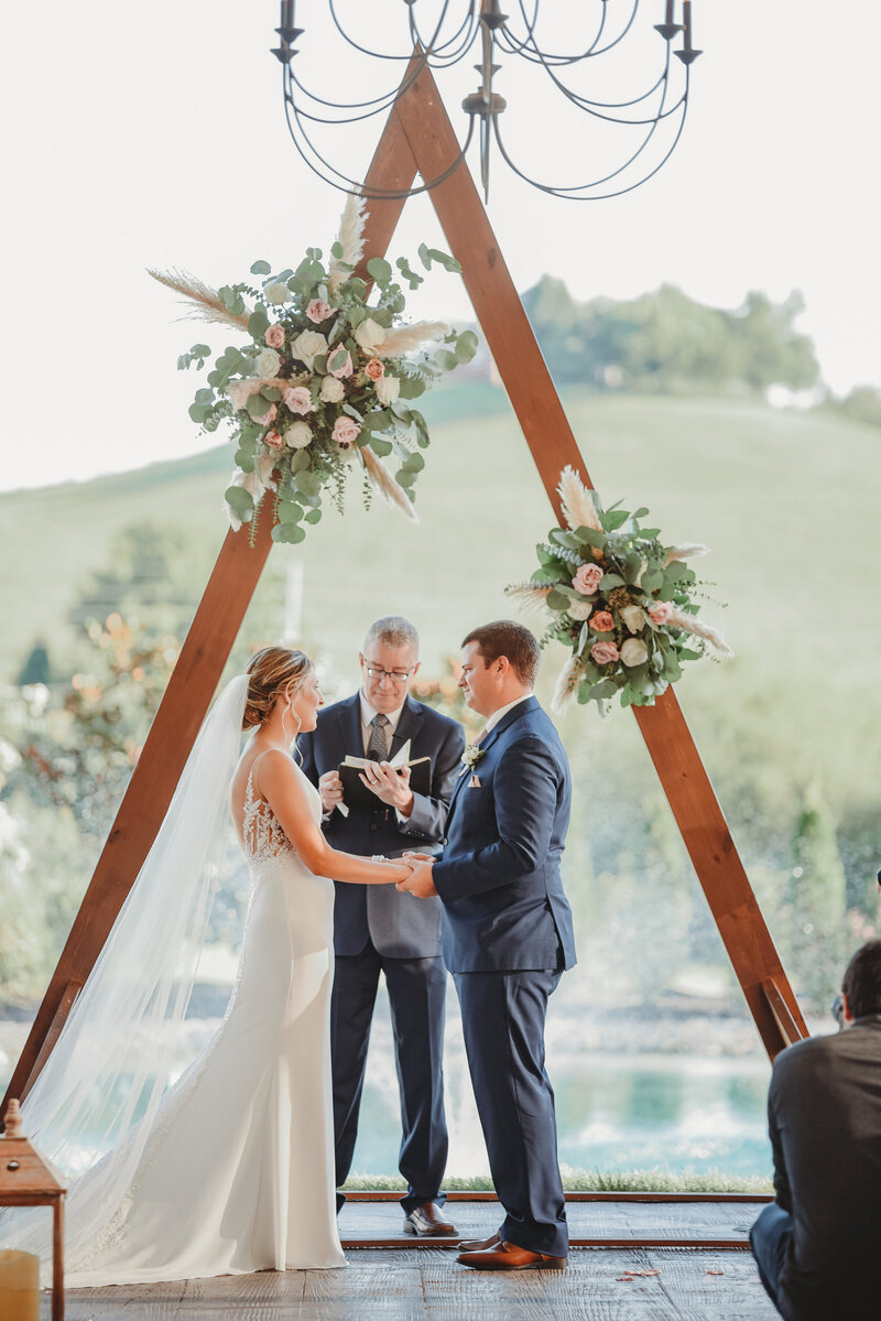 Couple exchanging vows under triangle wedding arbor at White Dove Barn