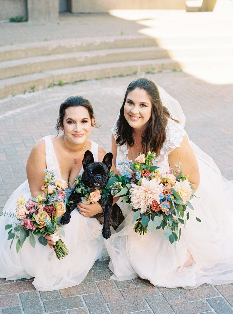 Brides kneeling down holding bouquets and black dog