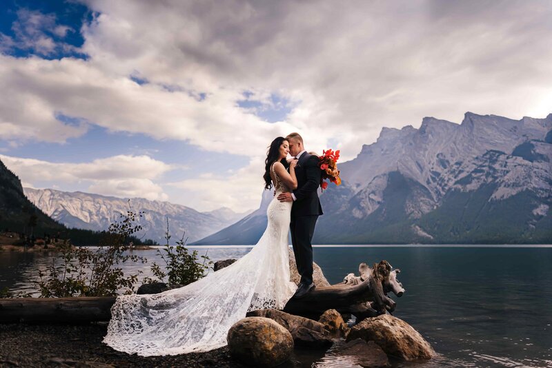 A picture-perfect moment of a newlywed couple captured at Lake Minnewanka, with the epic backdrop of the serene lake and majestic mountains.