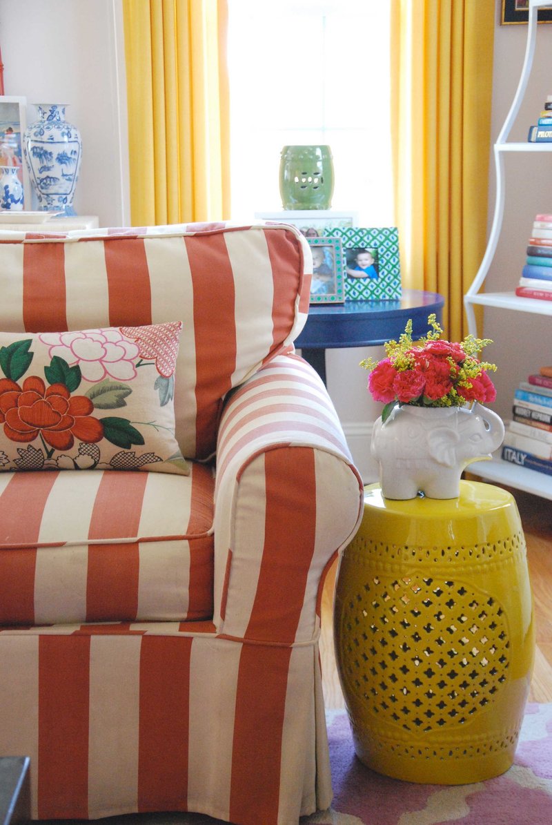 An orange and cream striped chair next to a yellow end table with an elephant vase.