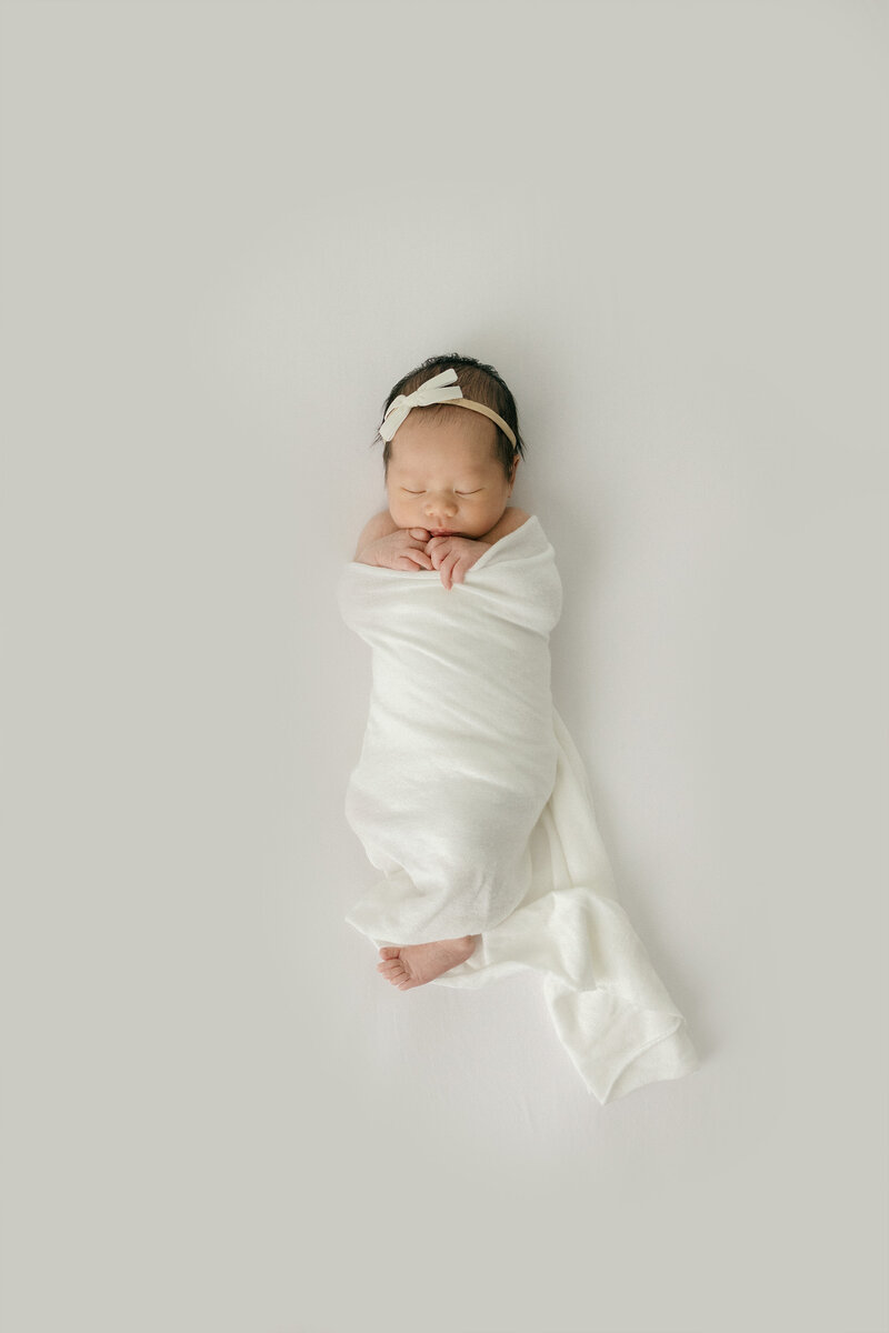 Newborn with bow on her head with all white background by New Jersey baby photographer