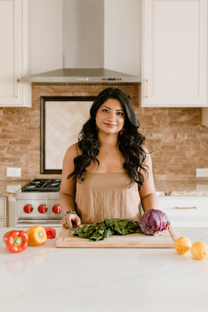 Nutrition coach Radhika standing in a kitchen with vegetables on countertop