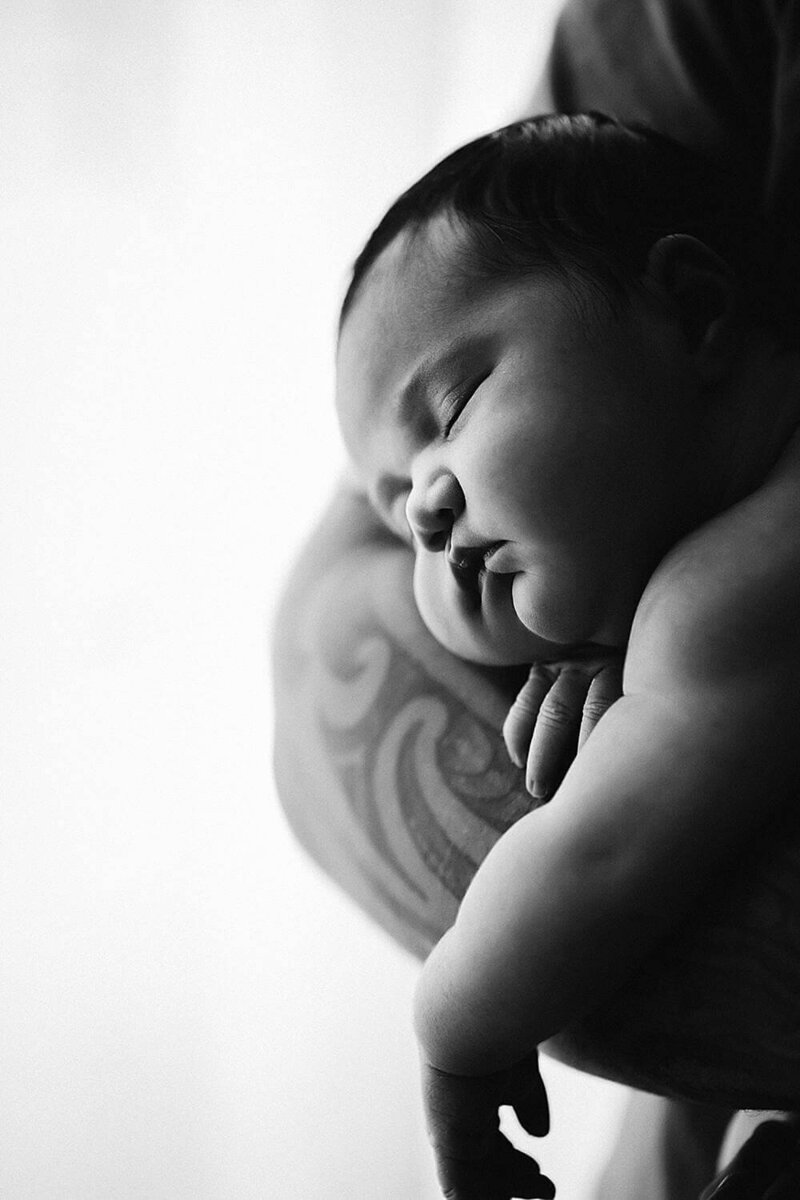 newborn baby being craddled in his fathers tattooed arms during a newborn photoshoot in new plymouth with aimee kelly photography