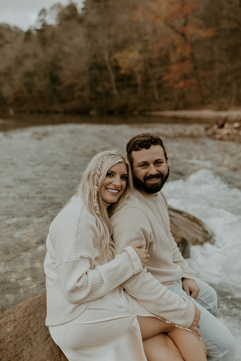 Couple smiling at the camera while sitting on a rock in the river