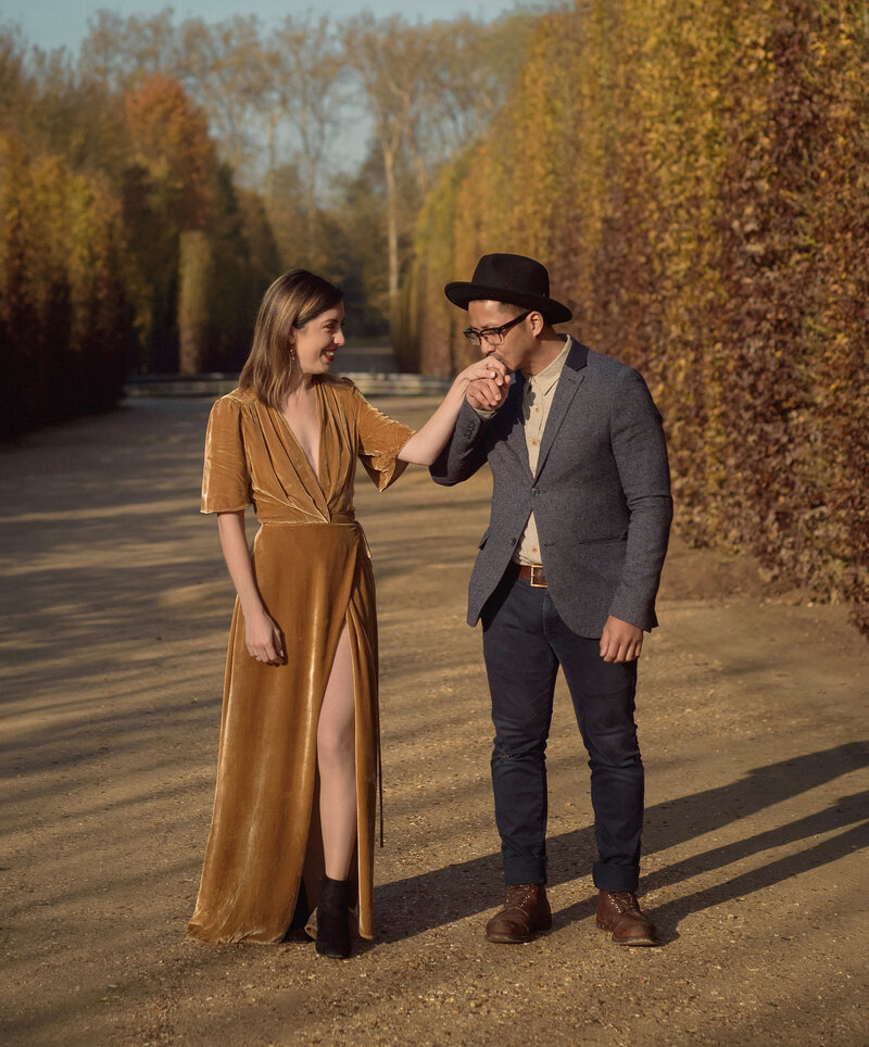kaylyn leighton and joe sinthavong in the gardens of versailles for their fall engagement session. women in gold velvet dress and hand being kissed.