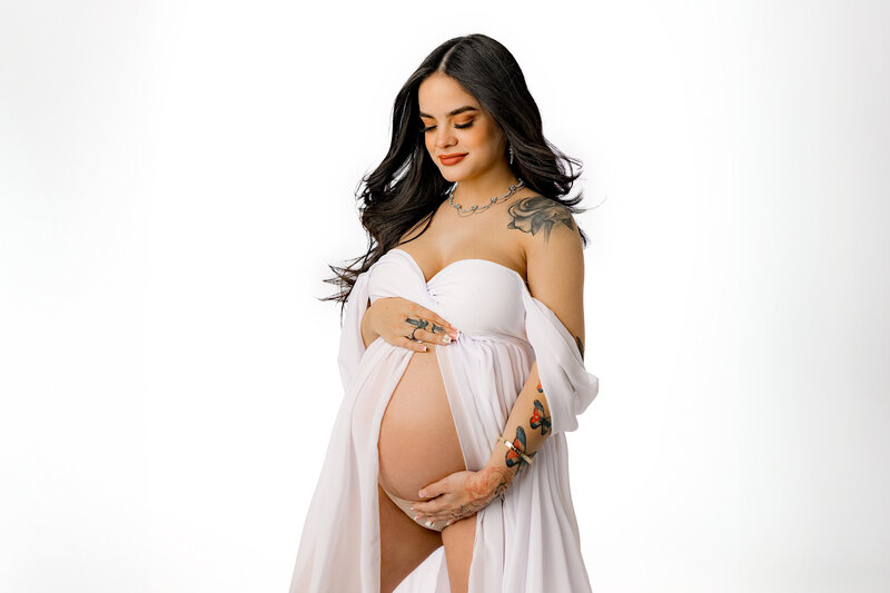 expectant mother looks down at her belly during wearing a white dress with her belly exposed