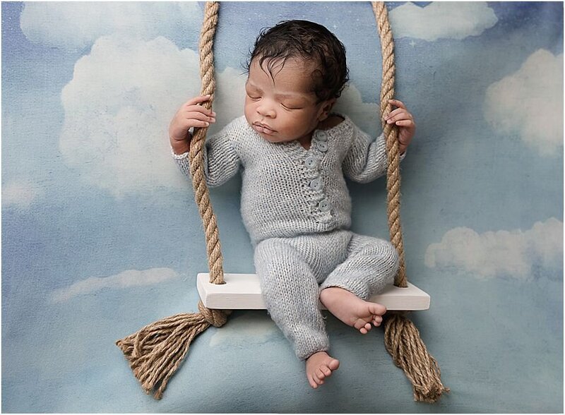 baby boy wearing blue romper on a swing in the clouds