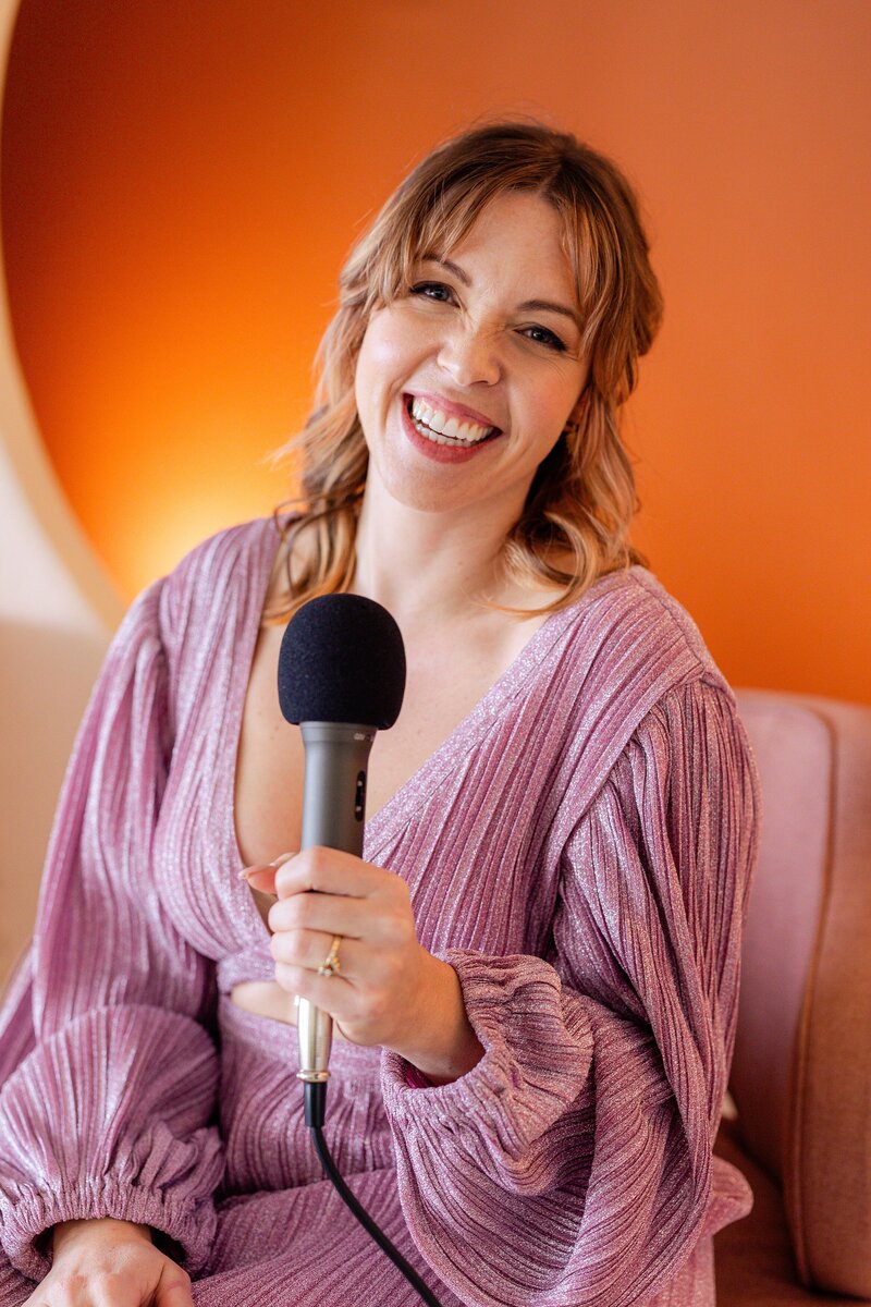woman in pink dress holds microphone for fun, energetic podcast marketing photos