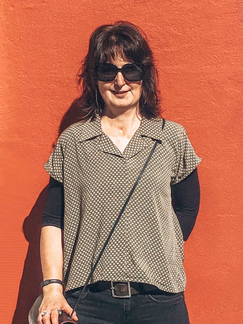 Lynda standing in front of red wall in Dunedin, New Zealand in home sewn shirt.