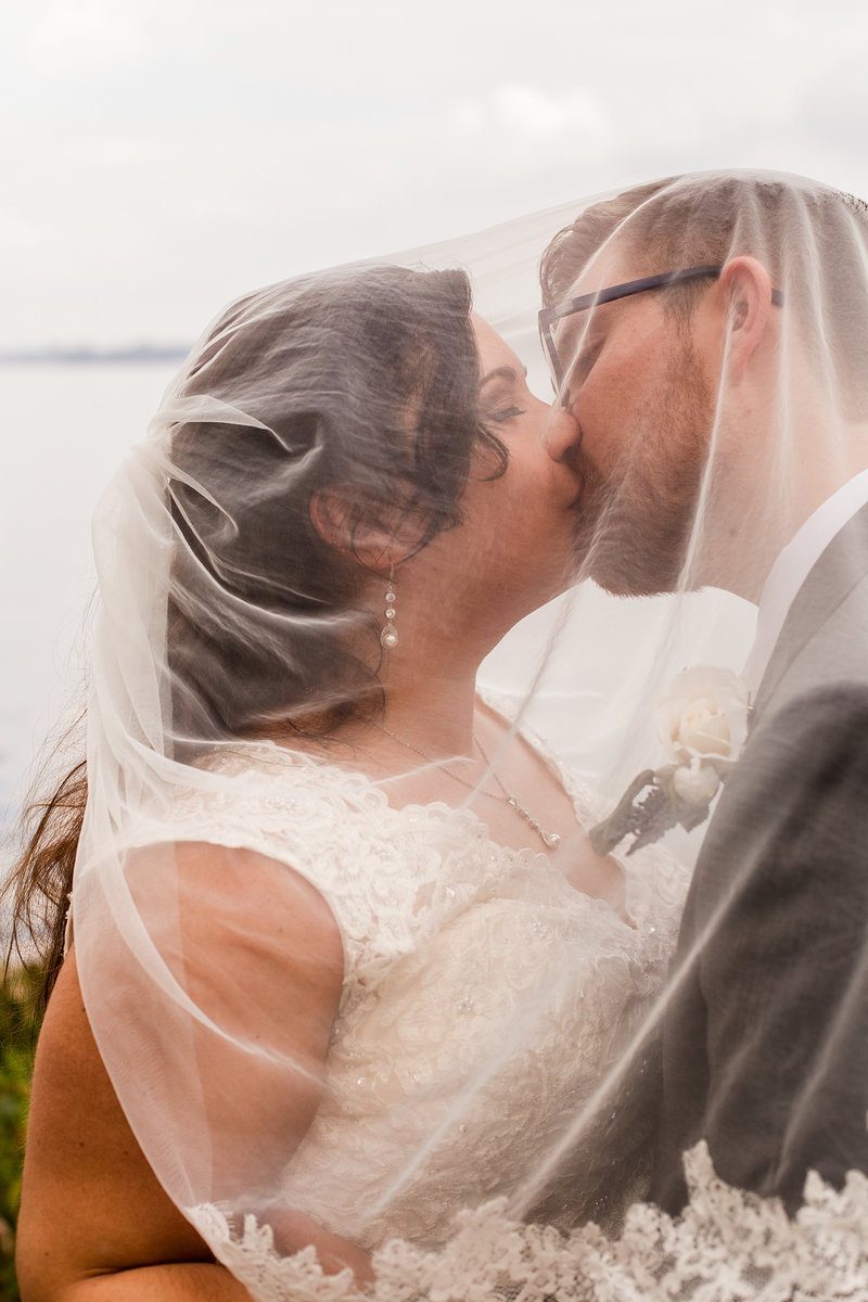 Bride and groom kiss under bride's veil along Lake Erie