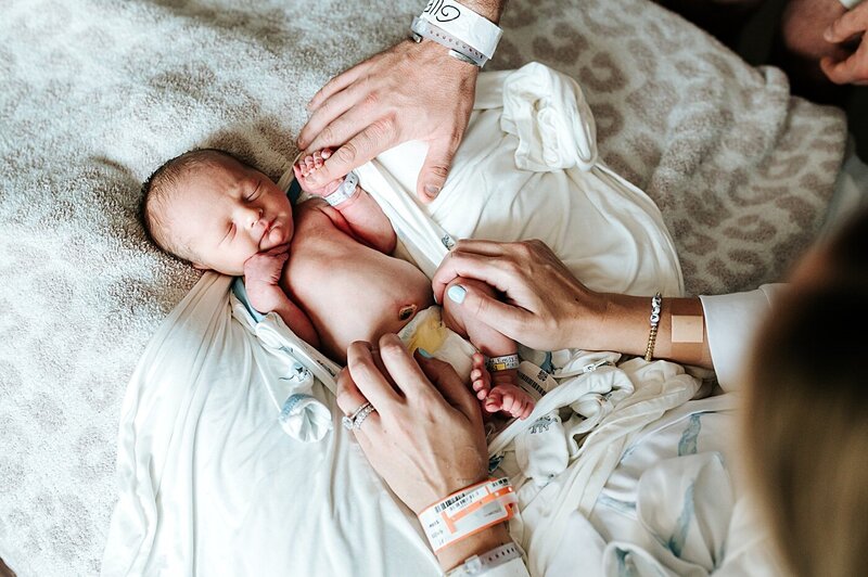 newborn baby in hospital bed with parents hands holding hom