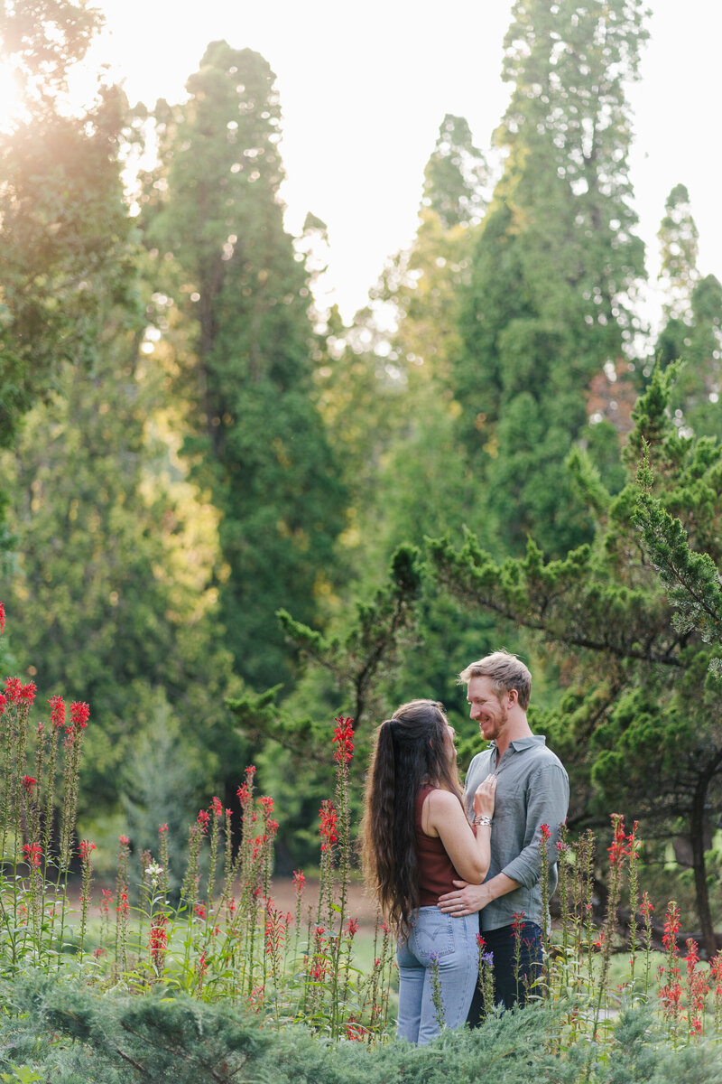 Brunette couple poses close together at Blandy Farm in Front Royal for their engagement photos, surrounded by bright blooms of a Virginia summer.