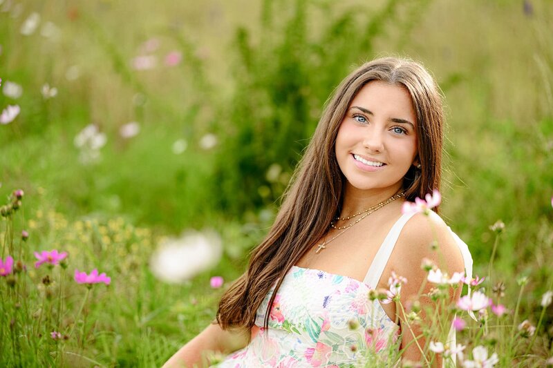 marvin ridge senior girl sits in a floral dress surrounded by flowers for her charlotte portrait session