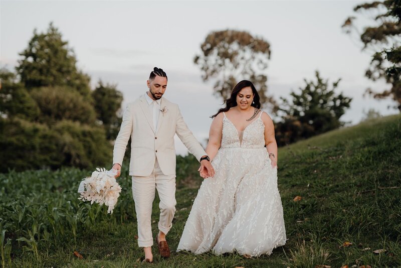 A newly married bride and groom walking in the fields at Narrows Landing a popular Hamilton wedding venue with waikato photographer Haley Adele