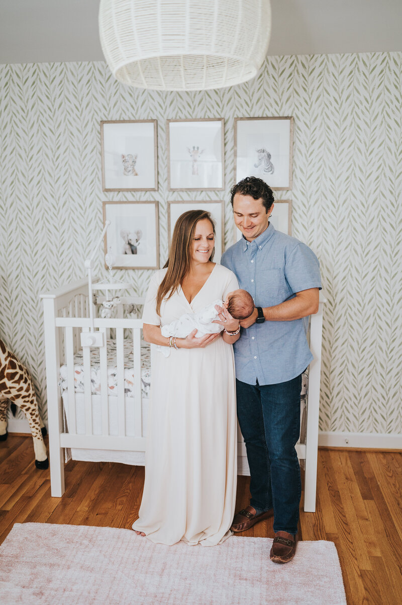 Mom and dad smile holding newborn baby girl during in-home photography session by Worth Capturing