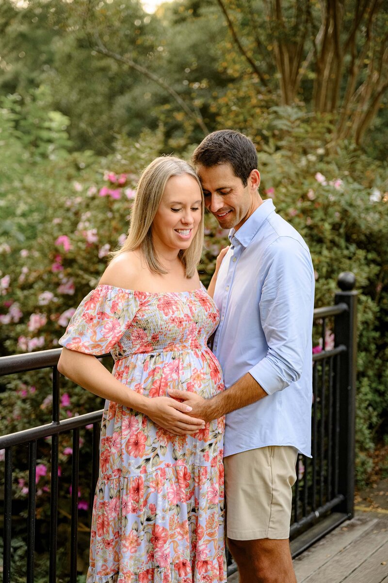 pregnant couple touches belly as  the lean together smiling