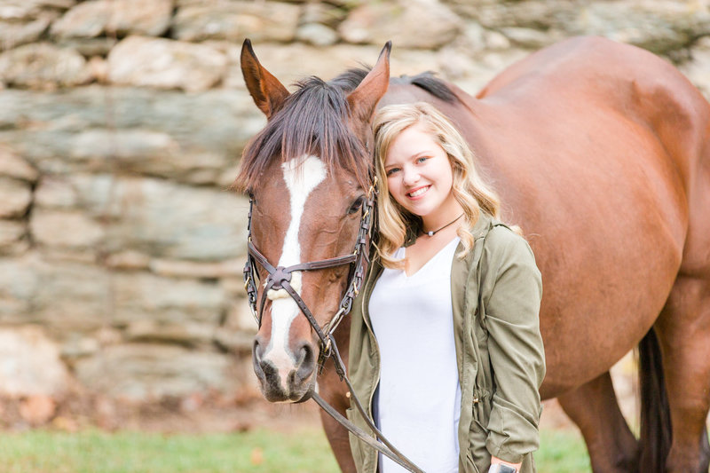 High school senior girl smiles for photo with her beautiful horse outside