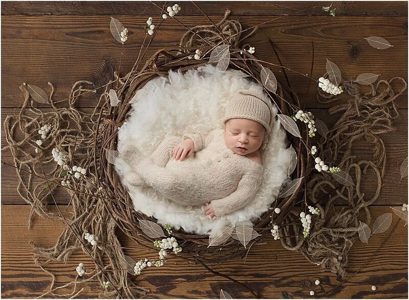 newborn baby wearing knitted romper and sleepy hat on a rustic nest