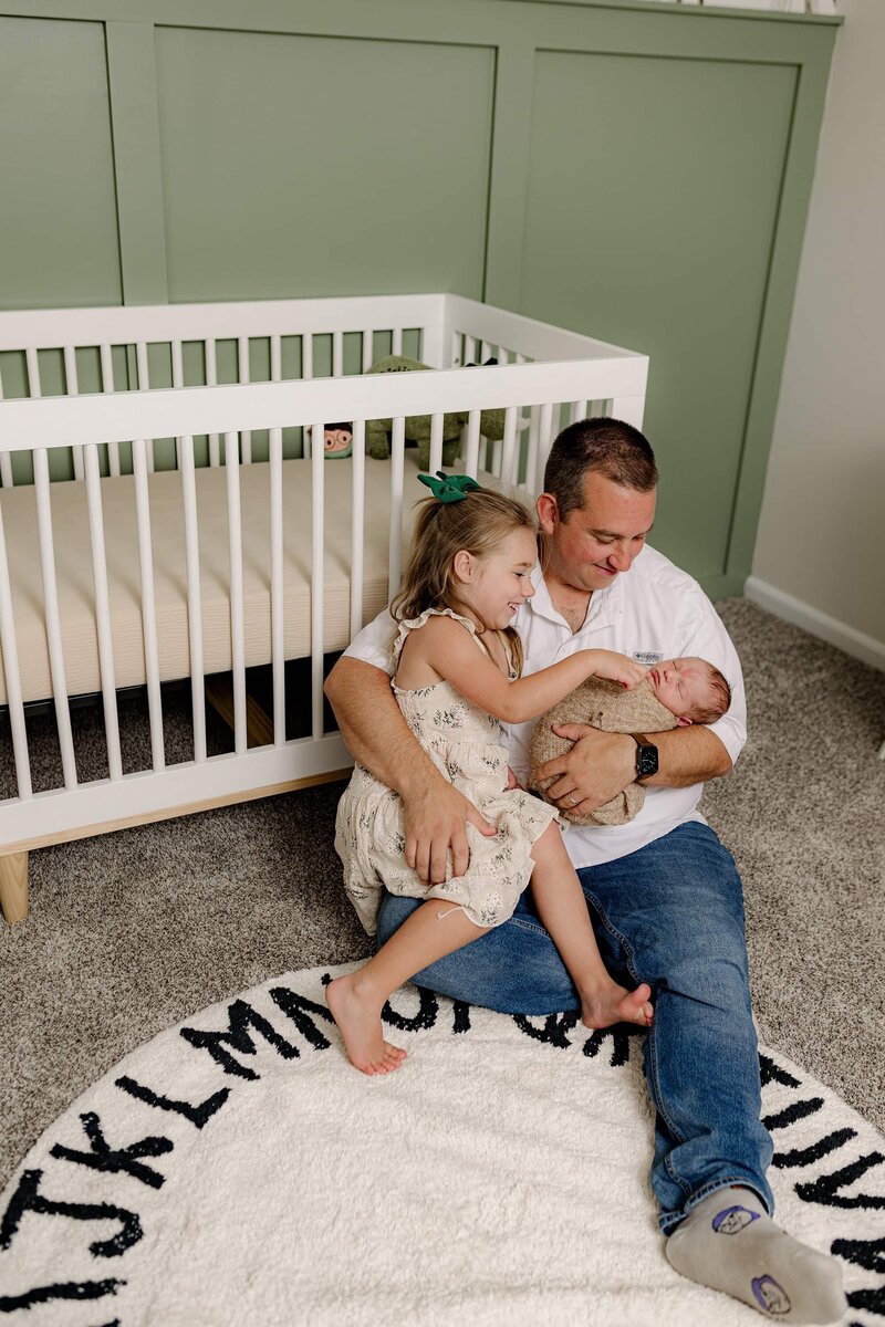 father snuggles both of his children while sitting in the flower of his son's  nursery