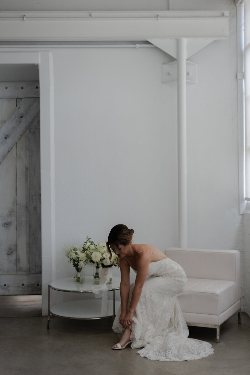 Bride putting on shoe while sitting on leather chair during getting ready photos at Blanc Denver