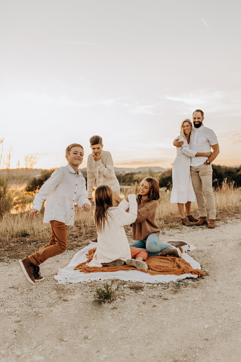 A family of 6 gathered on a hillside for a playful, candid photo.