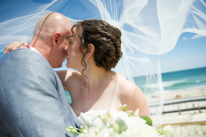bride and groom laugh under veil at beach