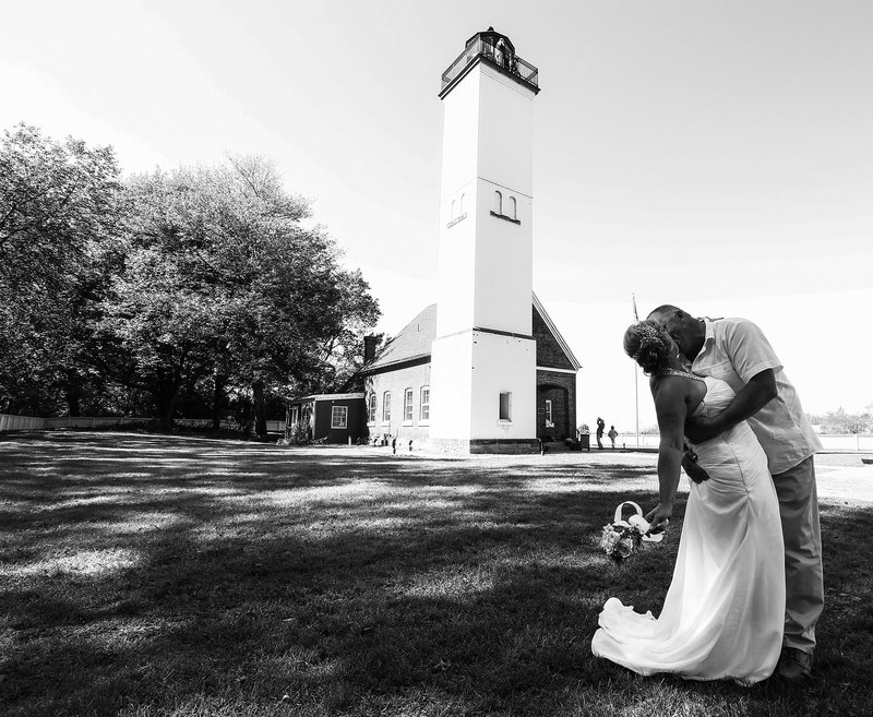 Bride and groom kissing  in front of lighthouse on Presque Isle State Park