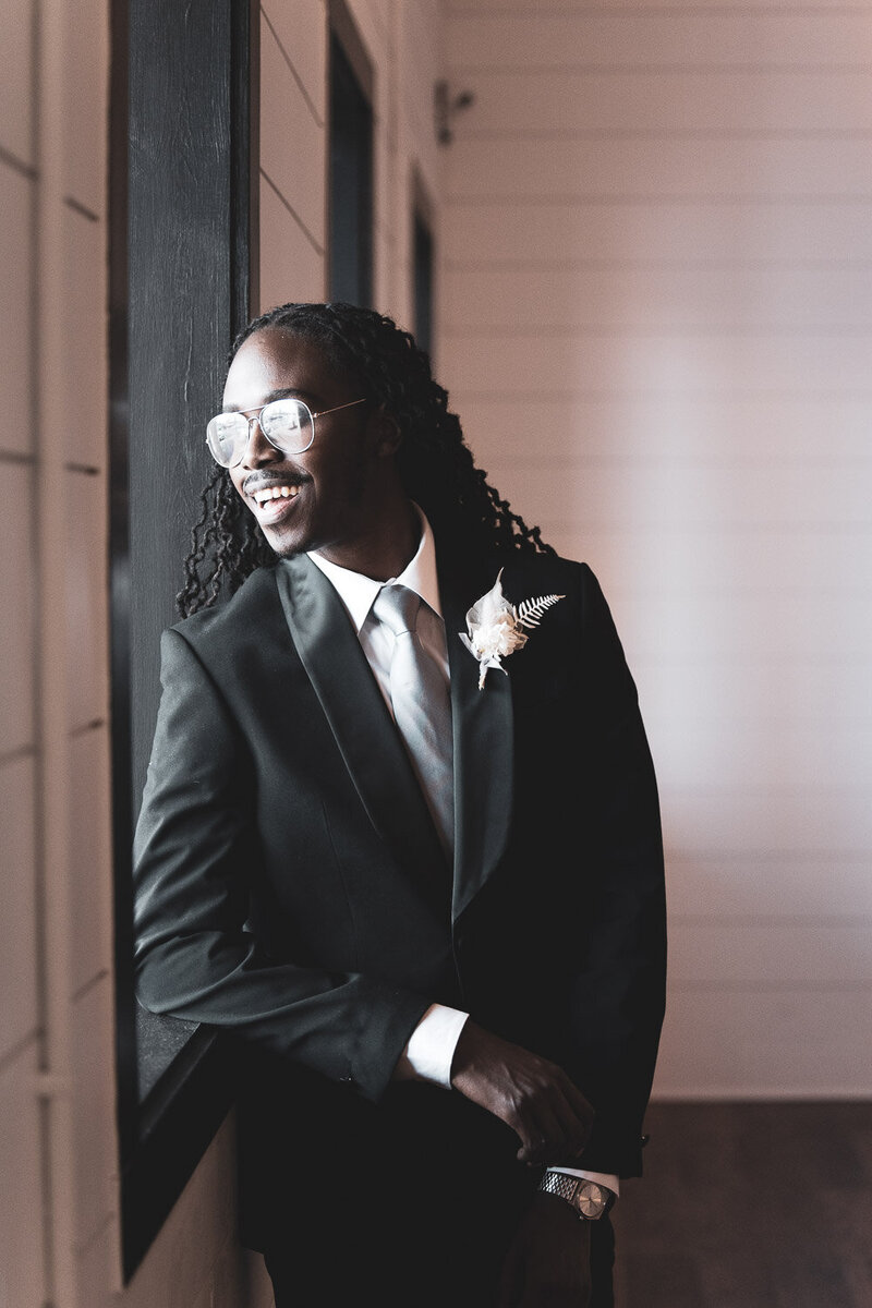 Black Groom in Tux looking out the window at Bash: Modern Event space By Indianapolis Wedding photographer | GreenPoint Photography