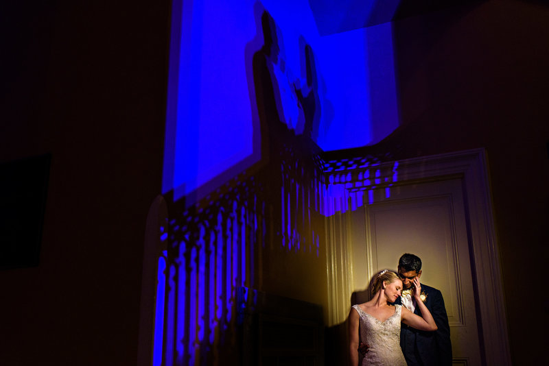 A bride and groom have a moment in the corner of their venue while the party keeps going.