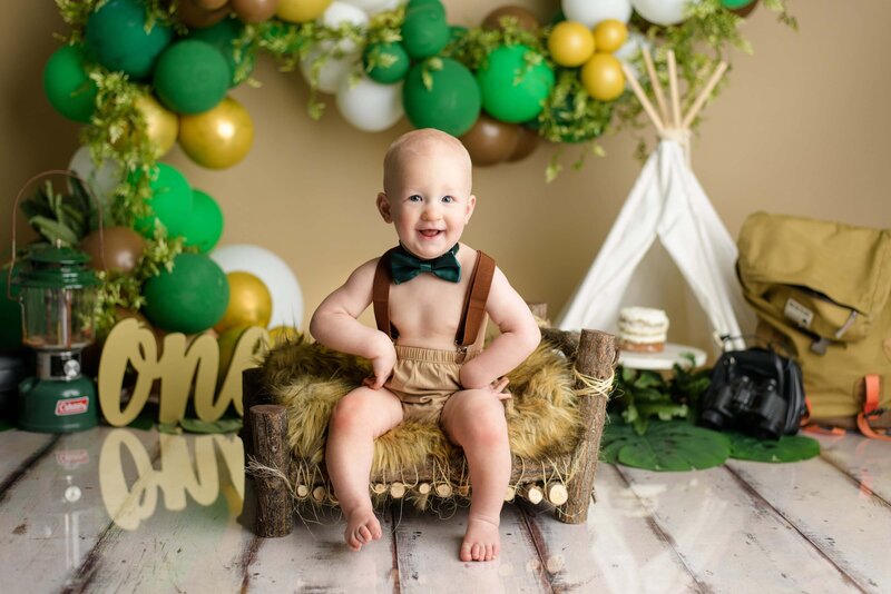 one year old boy sits on brown bench with hands on his hips during his studio cake smash session
