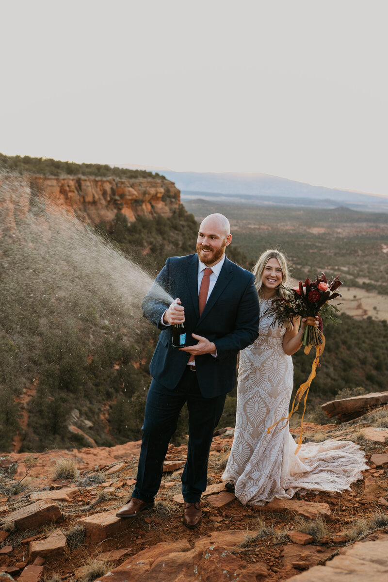 Bride and groom shake and shoot champagne bottle on Arizona mountaintop