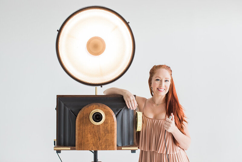 A redhead next to a tintype style vintage themed photo booth