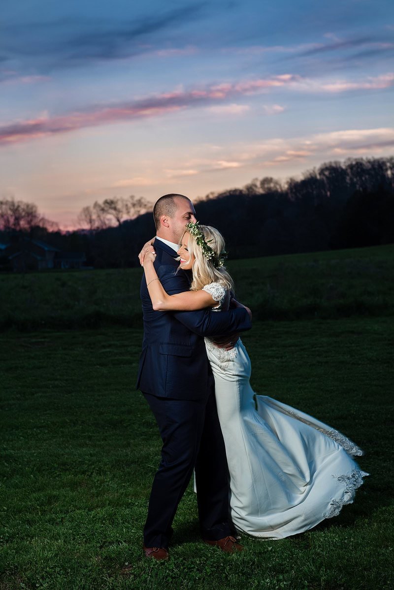 Groom picking up bride and spinning her around under the blue and purple sunset